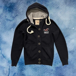 Mörkblå hoodie från Hollister - Otroligt snygg vintage Hollister Kofta med knappar | Storlek S men upplevs vara lite mindre i storlek, Längd 61cm , Bredd armhåla-amrhåla ≈ 46cm. Modell 175cm, 70kg | Hör av vid fler funderingar! 