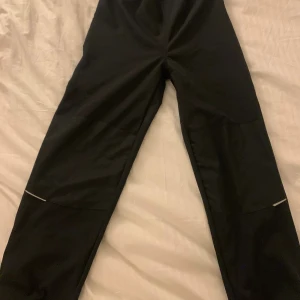 Svarta täckbyxor med reflexdetaljer - Svarta täckbyxor från Name It med elastisk midja och knappstängning vid benslut. Byxorna har reflexdetaljer på benen och är tillverkade i ett slitstarkt syntetmaterial som passar perfekt för kalla dagar. Snygg och enkel design som funkar till många olika stilar. Dem är max använda 3 gånger. Hör av er vi pris förslag o annat!