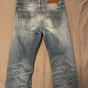 Blå Tiger Of Sweden jeans - Snygga Tiger of sweden jeans i ljusblå tvätt med klassisk femficksdesign och raka ben. Jeansen har slitningar och kontrastsömmar, samt läderpatch bak i midjan. Perfekt passform och cool faded look.