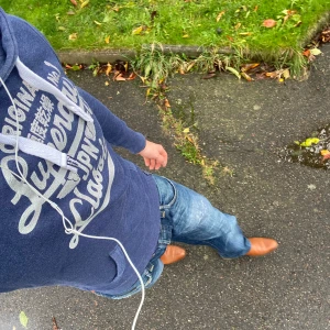 Superdry hoodie  - Säljer en marinblå hoodie från Superdry med stort vitt tryck på bröstet och klassiska snören i huvan. Tröjan har känguruficka, ribbade muddar och är tillverkad i mjuk bomullsmix. Perfekt för chill dagar eller när du vill ha en sportig look. Om du undrar något är det bara att skriva, priset är inte hugget i sten✅🙌