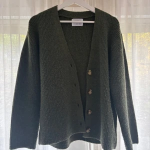 Mörkgrön stickad kofta från Zara - Mysig mörkgrön stickad kofta från Zara med v-ringning och snygga knappar framtill. Koftan har långärmad design och är perfekt för lager-på-lager-stil under kyliga dagar.