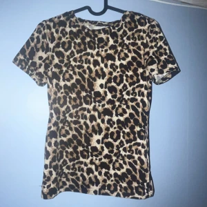 Leopardmönstrad t-shirt från Vera & Lucy - Säljer en snygg t-shirt från Vera & Lucy i storlek S med leopardmönster. T-shirten har korta ärmar och är i mjukt, stretchigt material. Färgerna går i beige, brun och svart, vilket ger en cool och trendig vibe. Perfekt för dig som gillar djurmönster och vill sticka ut.