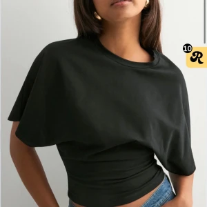 Svart croppad topp med vida ärmar - Säljer en svart croppad topp med vida, korta ärmar och rund halsringning. Toppen har en tight passform över midjan och är tillverkad i mjuk bomull. Perfekt för dig som gillar en stilren och trendig look. Från missay