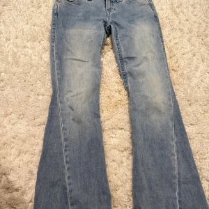 True Religion Joey Low Rise Flare Jeans - Snygga ljusblå jeans från True Religion, modell Joey Low Rise Flare. De har låg midja, utsvängda ben och klassiska fickor med lock och knapp bak. Tillverkade i mjukt denim med coola slitningar för en avslappnad vibe.