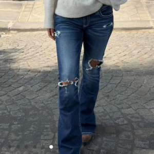 Trendiga slutsålda jeans  - Slutsålda från gina. Använda max 3 gånger! Snygga blå bootcut jeans med slitna detaljer och hål på knäna. Jeansen har kontrastsömmar och dekorativ broderad bakficka. Tillverkade i klassiskt denimtyg. 