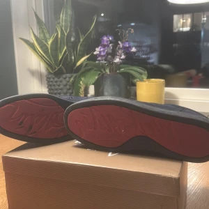 Christian Louboutin Louis Strass sneakers - Säljer ett par mörkblåa Louis Strass sneakers från Christian Louboutin i mocka med klassisk röd sula. Skorna har rund tå, svarta snören och lyxig känsla. Perfekta för dig som vill sticka ut med exklusiva detaljer och ikonisk design.