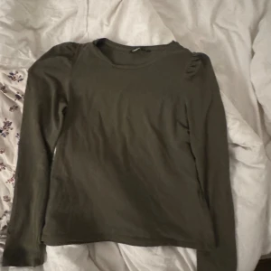 Olivgrön långärmad tröja från ONLY - Olivgrön långärmad tröja från ONLY med rund halsringning och diskreta puffdetaljer vid axlarna. Tröjan är i mjuk bomull och har en enkel, clean look som passar perfekt till jeans eller kjol.