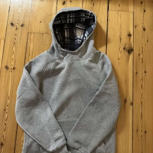 Grå hoodie med rutigt foder i huvan - Säljer en enkel och stilren grå hoodie med rutigt foder i huvan. Aldrig använd 