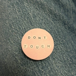 Rosa popsocket med texten 'DONT TOUCH' - Säljer en rund rosa popsocket med texten 'DONT TOUCH' i silverfärgade bokstäver. Baksidan har självhäftande tejp från 3M för enkel fastsättning på baksidan av sin mobiltelefon. Perfekt accessoar för att uttrycka din personlighet.