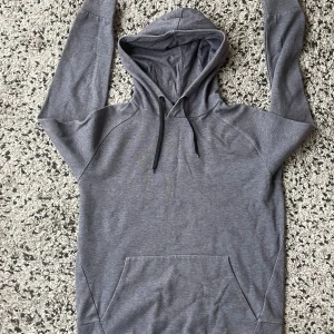 Grå hoodie från SOC med huva - Snabb leverans. Säljer en stilren grå hoodie från SOC med svart snörning i huvan och magficka. Tröjan är i mjuk bomulls- och polyestermix, perfekt för chill dagar eller när du vill vara bekväm. Klassisk passform och långärmad modell.