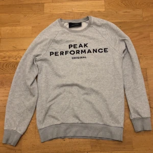 Grå sweatshirt från Peak Performance - Säljer en stilren ljusgrå sweatshirt från Peak Performance med svart broderad logga på bröstet. Tröjan har rund hals, ribbade muddar och är tillverkad i mjuk bomullsmix. Perfekt för en chill och sportig look. Pris kan diskuteras!