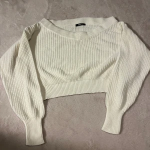 Vit croppad stickad tröja Gina Tricot - Superfin vit croppad stickad tröja från Gina Tricot med bred ribbad struktur och lång ärm. Tröjan har en snygg v-ringning och breda muddar vid ärmslut och nederkant. Perfekt att styla med höga jeans eller kjol.