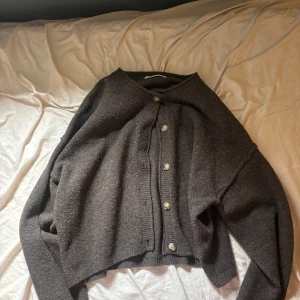 Mörkgrå kofta från Pull&Bear - Mysig mörkbrun kofta från Pull&Bear i storlek S. Koftan har långa ärmar, rund hals och knäppning med fem ljusbruna knappar framtill. Materialet är stickat och ger en chill och avslappnad vibe, perfekt att slänga på sig när det är lite kyligt.