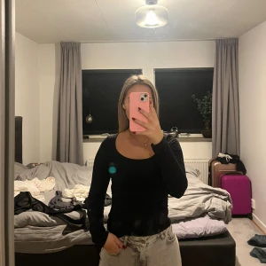 Svart långärmad topp med rund hals - En svart långärmad topp med rundad halsringning. Modellen är slim och sitter snyggt mot kroppen. Perfekt att matcha med jeans eller kjol för en clean och enkel look. Materialet känns mjukt och stretchigt mot huden.