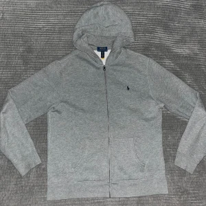 Grå zip hoodie från Polo Ralph Lauren - Snygg grå hoodie från Polo Ralph Lauren med dragkedja och huva. Tröjan är ny och inga defekter. Tröjan xl i barn storlek så funkar perfekt om du har s men också m