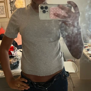 Grå croppad stickad topp - Säljer en ljusgrå croppad stickad topp med korta ärmar och rund hals. Enkel och clean design som är lätt att matcha med jeans eller kjol. Mjuk och skön kvalitet, perfekt för dig som gillar minimalistisk stil.