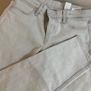 Ljusgrå jeansbyxor med raka ben - Säljer ett par ljusgrå jeansbyxor med klassisk femficksdesign och raka ben. Byxorna har bälteshällor och är sydda i ett mjukt bomullstyg med en stilren look. Perfekta för dig som gillar en enkel och clean stil.