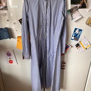 Randig klänning strlk M - Blåvit-randig skjortklänning med knytband i midjan. Slutar vid mina vader och jag är 170cm. Köpt på asos. Tight passform på överkroppen sen är ”kjolen” luftig.
