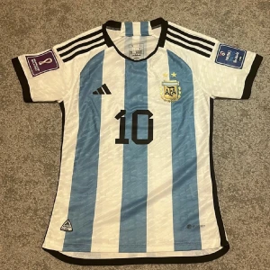 Argentina Fotbollströja - En Argentina Fotbollströja 2022 med Messi 10 och alla patches. Tröjan är players edition vilket är den dyrare varianten. Den är bara använd några gånger och därmed inte skadad på något sätt.