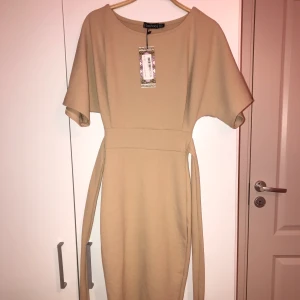 Nude klänning med band vid midjan - Säljer en nude tajt klänning för 200kr 🤩 Köpt från boohoo (beställde flera storlekar). Klänningen är i nyskick, aldrig använd, taggarna är kvar. Plagget har en pösig överdel och ett band vid midjan, därefter sitter den tajtare på underdelen. Finns äve