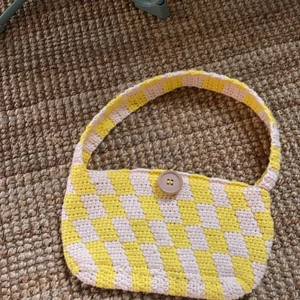 Virkad handväska - Säljer en jättesöt väska som jag virkat själv! Gul- och vitrutig med en träknapp på, bra garn i bomull.   Säljer även i andra färger på beställning 🥰