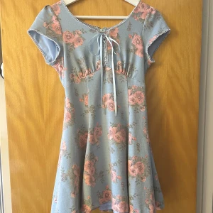 Blommig klänning - Otroligt drömmig klänning 😍💙 Med spets pch rosettdetaljer. Snöras upp med band. Dragkedja där bak. Lite längre än mitten av låren. Insidan är lined med silke 🤍