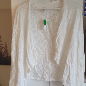 Kofta med spets - En vit supergullig kofta med spets på ryggen och även ärmarna! Slutet på ärmarna vidgas ut vilket visas på bild 2.  Helt oanvänd, prislappen sitter kvar.  Storlek XS  Köptes för 199 säljer för 80 kr.