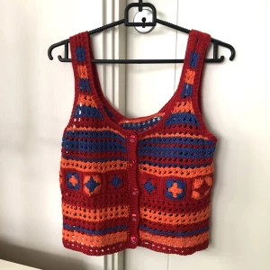 Skickat linne - INTE ANDVÄND. Sticks inte. Ett rött, orange och mörkblått linne från Zara. Stickad och med röda knappar som går att öppna på framsidan. Randigt mönster med ett mindre mönster av stjärnor i mitten.