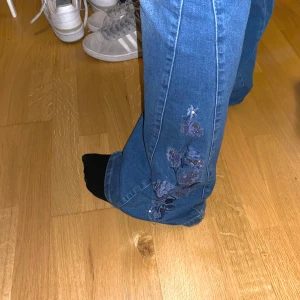 Bootcut Jeans  - Assnygga bootcut jeans med coola blommor på båda benen längst ner. Mörkblåa i storlek 42! Medium höga i min midja. Jag är 162 cm! 