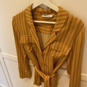 Samsoe samsoe blus/skjorta Karin shirt aop  - Vacker blus/skjorta från samsoe samsoe med knytskärp i midjan. Flerfärgad/randig i glansigt silkes material. Går fint att bära både med eller utan skärp i midjan. Köpt för 1,399kr. Varan är i mycket gott skick, endast använd 2 gånger.   Kan postas :) 