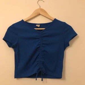 HM topp - Snygg, blå, ribbad topp som är hopdragen därframme. Ej använd särskilt mycket.