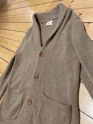 NN07 - ullkofta  - Härlig ullkofta från NN07. 80% lammull. Stora fina träkknappar. Bilderna är inte riktigt rättvisa och är mer beige i verkligheten.  Står XL men är mer som medium/large