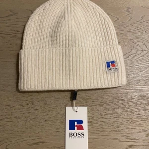 Hugo Boss mössa ONE SIZE - Nyinköpt vit mössa från Hugo Boss. Endast testad med lappen kvar. Säljer pga att den inte kommer komma till användning. Köpt för 879kr.