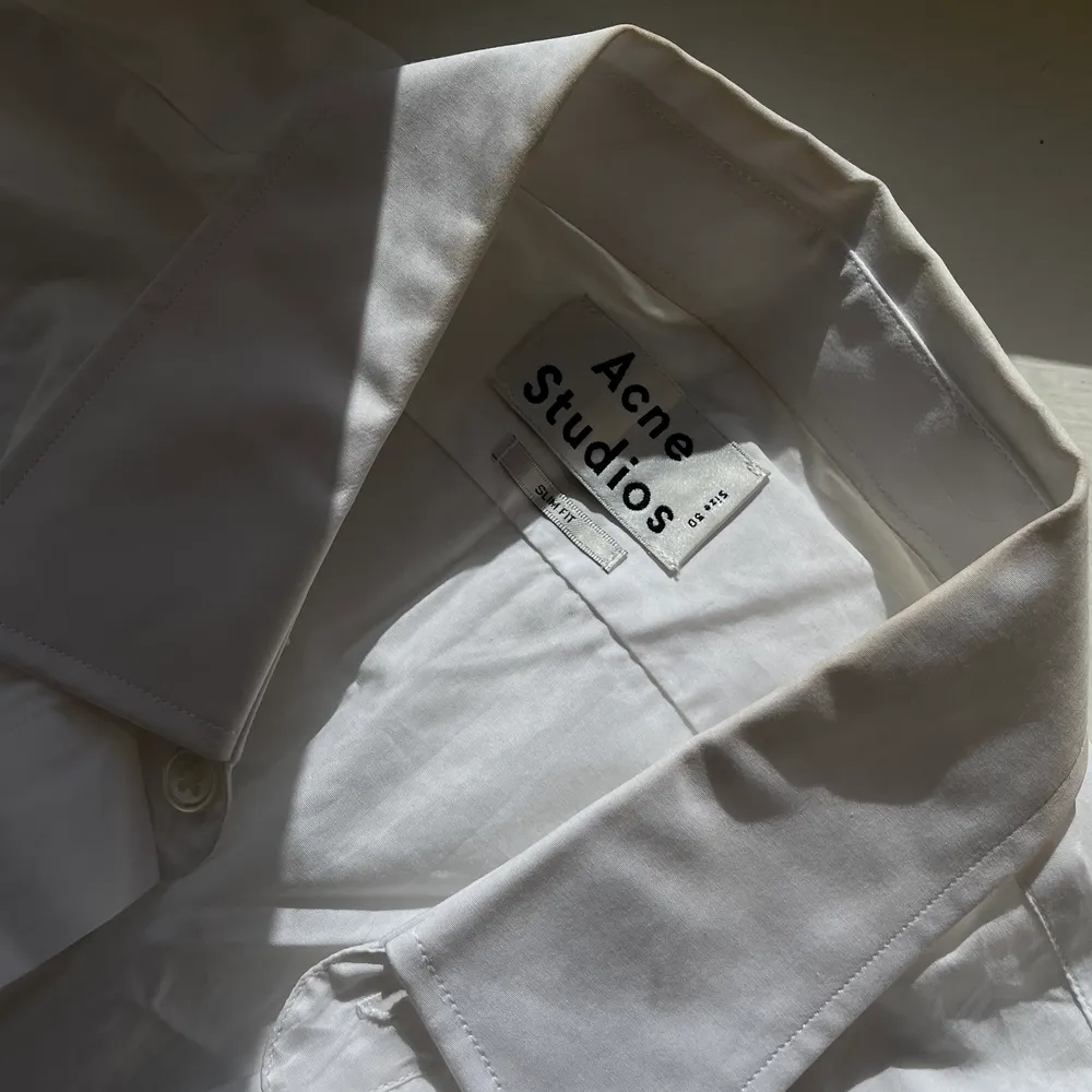 Kortarmad vit skjorta med knappar och krage från Acne. Skjortan har en rak passform och det går lätt att bli av med det skrynkliga genom strykning eller steamning. Plagget är i fint skick. Storlek medium men är oversized och funkar bra på en small eller large. Säljer vidare för 550Kr. . Skjortor.