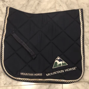 Mountain Horse dressyrschabrak - Marinblått Mountain Horse dressyrschabrak till salu. Mycket fint skick. Storlek ponny, använd på liten C-ponny. Broderad Mountain Horse-logga på en sida. 