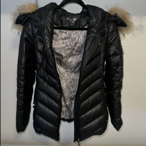 Hollies vinterjacka med päls på luva - Hollies vinterjacka med pälsluva, håller väldigt varmt, har bälte i midjan ifall man vill forma midjan men kan tas av. sparsamt använd så inga defenkter, kan dock vara lite smutsig men inget som märks mkt. Nypris 3500kr