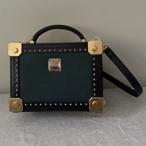 Rare MCM Berlin Handbag and Crossbody - Rare MCM Berlin Handbag and Crossbody  Beautiful Hard Luggage Shape with Golden MCM Hardware. Has some scuffs around edges but overall excellent condition   MCM Golden Push-lock fastening Closure. Interior flat pocket  Black Leather Trim with Dark Green Embossed Visetos Coated Canvas  Adjustable Black Leather Crossbody Strap, Removable  Single Black Leather Top Handle  An exquisite miniature of MCM’s finest hard luggage, the Small Berlin Crossbody is crafted in Odeon coated canvas for a structur