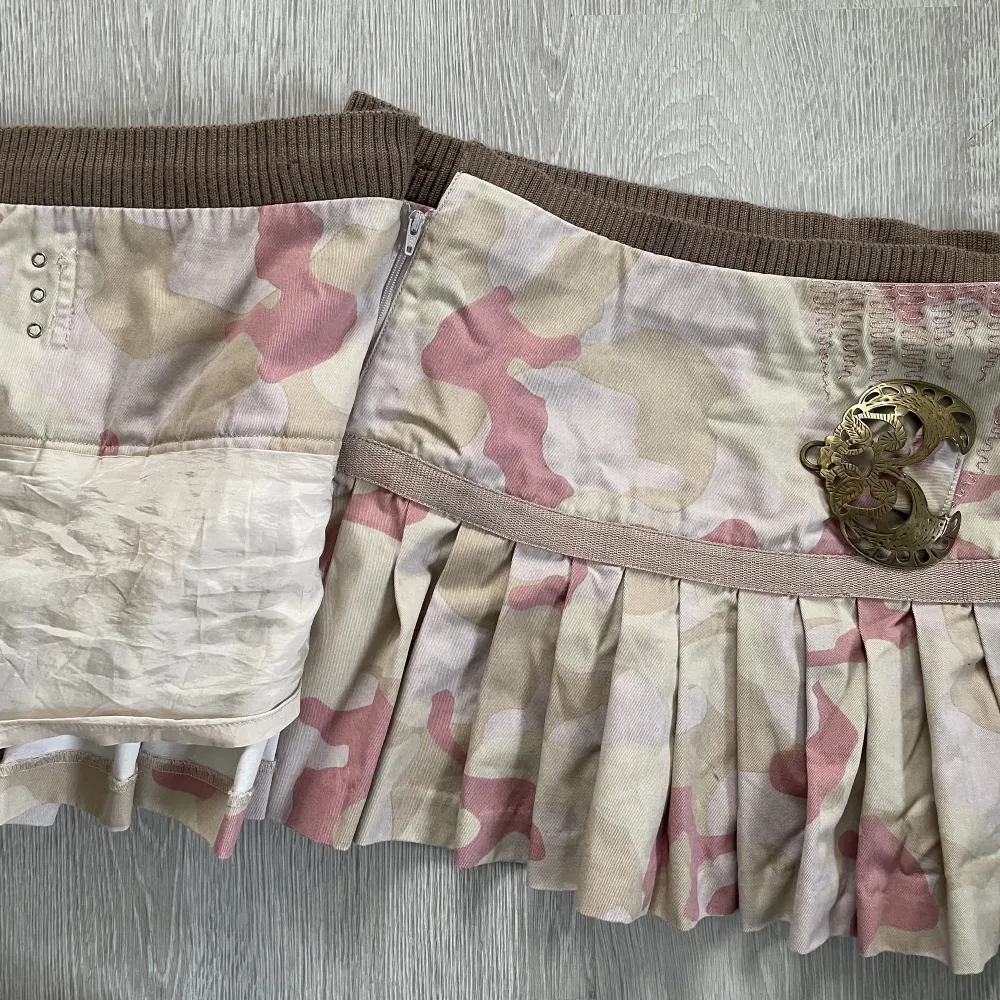 Perfekta vintage y2k kjolen från märket Munthe plus Simonsen💓 Rosa camo mönster, plisserad och har coolt fjärilsspänne och andra snygga detaljer🌸 Storlek på lappen är eu34, men skulle säga närmare 36, se mått: 39cm platt midja, 34cm längd🌟. Kjolar.