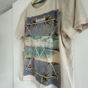 T-shirt med tryck - En beige t-shirt med ett tryck föreställt av en strand. Väldigt skönt material. Från Lindex kids. Storlek 170/XS. Pris kan diskuteras. Frakten ingår i priset. Endast betalning via Swish😊🌸