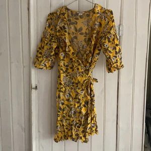 Superfin blommig wrap-klänning från Monki! - Somrig klänning från monki som knytes på ena sidan av kroppen. Mycket smickrande kort trumpetarm. Obs! Urringningen ser mycket större ut på bild och går att justera i hur tajt du knyter klänningen. Använd men ser fortfarande ut som ny!
