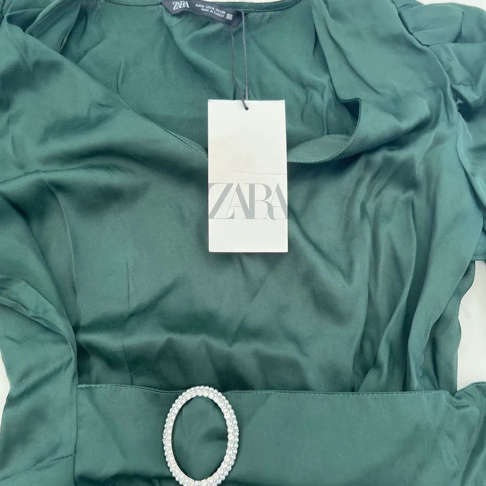 Vardaglig alternativ festlig topp från ZARA i en fin mörk grön färg säljes i storlek M. Prislapp sitter kvar. Perfekt silkestyg med ett stilrent bälte i mitten. . Blusar.