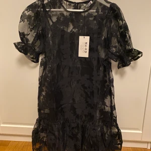 Svart klänning - OANVÄND! Svart klänning från NA-KD. Blommig transparent klänning med nedre volang. Underklänning hör till men går att använda var för sig! Köparen står för frakten 