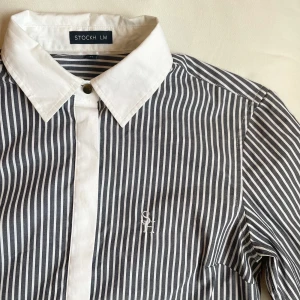 Tidlös Skjorta - Elegant skjorta i strl.34. Figursydd och ger en väldigt fräsch look. Gulddetalj översta knappen.  Köpt från MQ. Sparsamt använd.