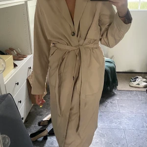 Kappa från Monki - Beige trenchcoat från Bikbok i storlek S. Knappt använd och är som ny.