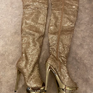 Gold sequin Pleaser boots - Pleaser lårhöga stövletter med peep toe. Storlek 36, i väldigt bra skick. Alla diamanter och paljetter finns kvar och sulan och klackarna är som nya. Kommer i kartong. OBS! Finns små skönhetsfel fram på stövlarna, se bild. Skorna är använda en gång inomhus. 