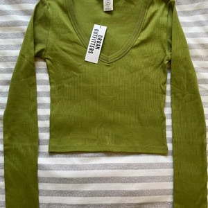 Urban Outfitters långärmad topp - En V ringad, grön topp med långa ärmar från Urban Outfitters. Den är i storlek S. Aldrig använt förut, och säljer den för att jag känner att den är för urringad för mig. Skriv om det är något ni undrar över.😊