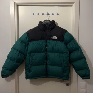 The North Face 1996 Retro Nuptse  - Välskött vinterjacka från The North Face i grönt, storlek L!  Jackan är köpt ny och enbart använts 1 vinter. Fri från fläckar och hål förutom ett minimalt ”skrap” på framsidan. Visar gärna ytterligare om önskas.  Midjan är justerbar. Passar därför även M.