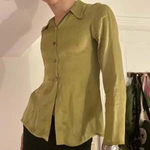Vintage grön satinskjorta slits - Vintage olivgrön satinliknande skjorta med de coolaste glansiga knapparna och slits på sidorna 🍃🌿🌱 Älskar att den ser så lyxig ut men samtidigt så effortless!!