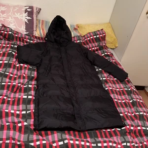 Lång svart Vinterjacka  - Lång svart vinterjacka. Det är storlek xs men den stor i storleken så du som har storlek M kan ta på dig den. Tål vatten och snö. Två fickor och en luva. Luvan kan tas bort. Super snygg på jätte bra kvalite. 