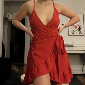 Röd omlott klänning  - En röd klänning från Gina Tricot som går omlott samt knyts i midjan! I strl 34 men justerbar eftersom man knyter den omlott själv så skulle passa både mindre o större! Volanger längst ner som gör den så gullig, samt passformen är perfekt 😊knappt använd! 